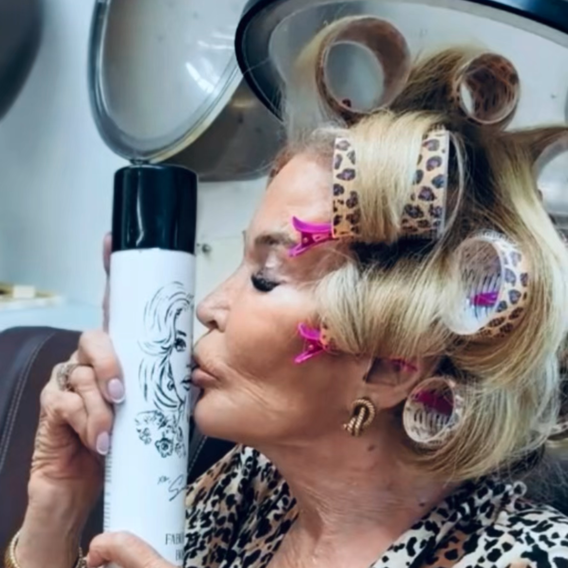 Woman with styled hair holding a bottle, wearing a leopard print outfit.